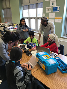 Parent Roy working with a group of students at a table helping them to build a robot at a after school club.