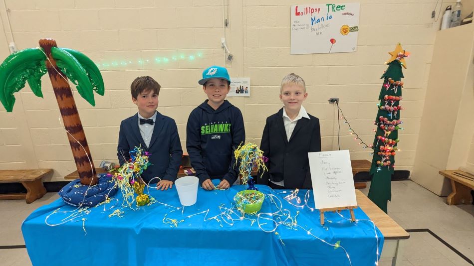 Three students at a table selling lollipops for student fundraiser.