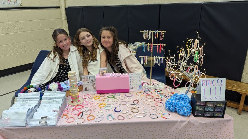 Three students at a table selling bracelets for student fundraiser.