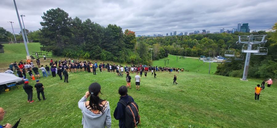  Hundreds of students are seen running down a grassy ski hill at the beginning of a cross country race.  