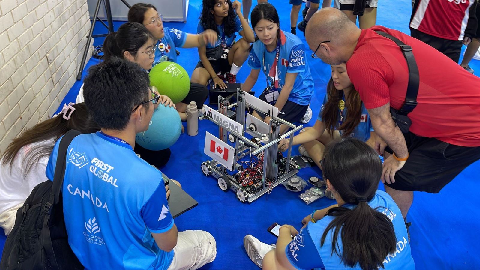 02 – Members of Team Canada and staff advisors surround their robot as it sits on the floor of the competition space.