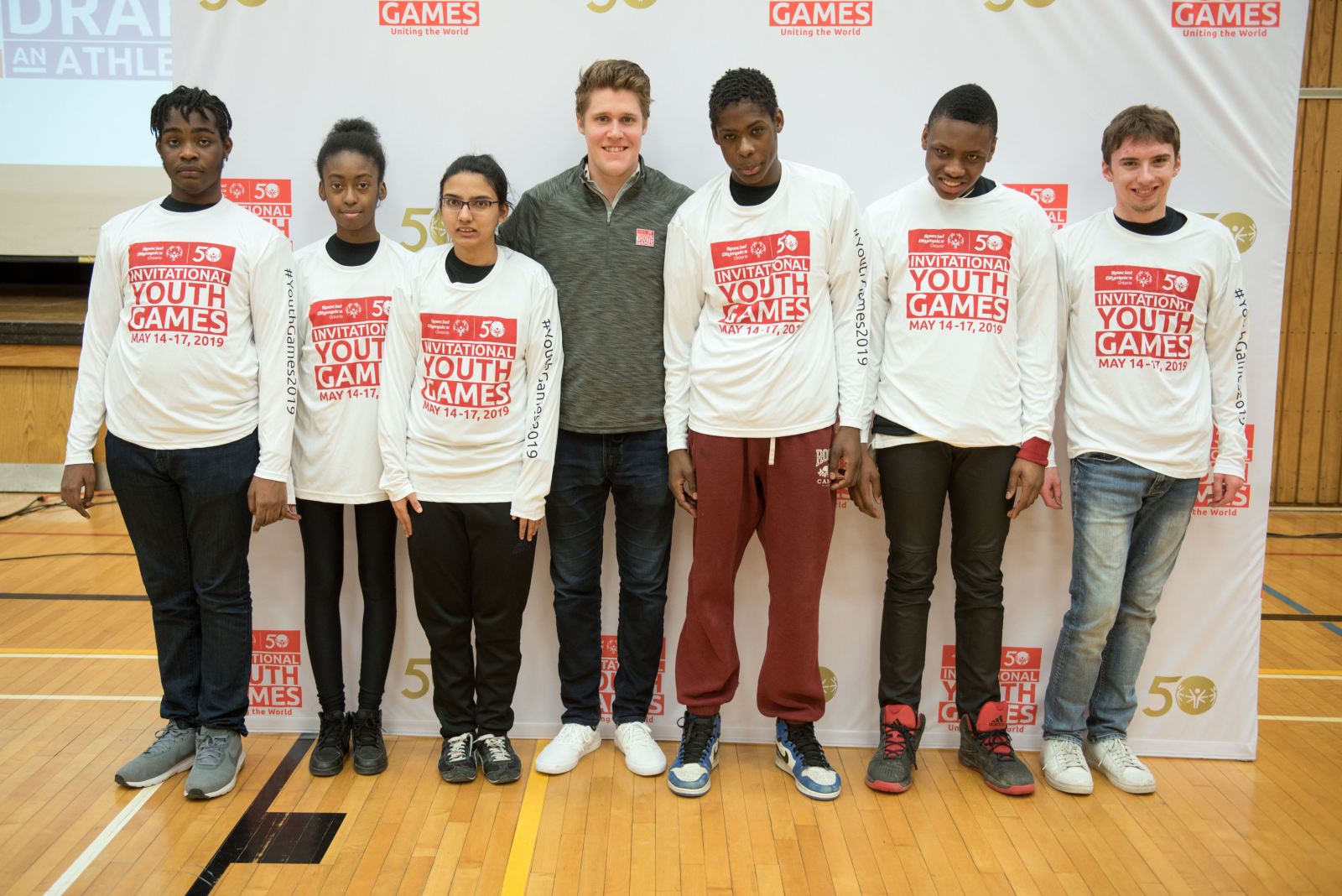 6 students posing in front of a branded backdrop with an adult
