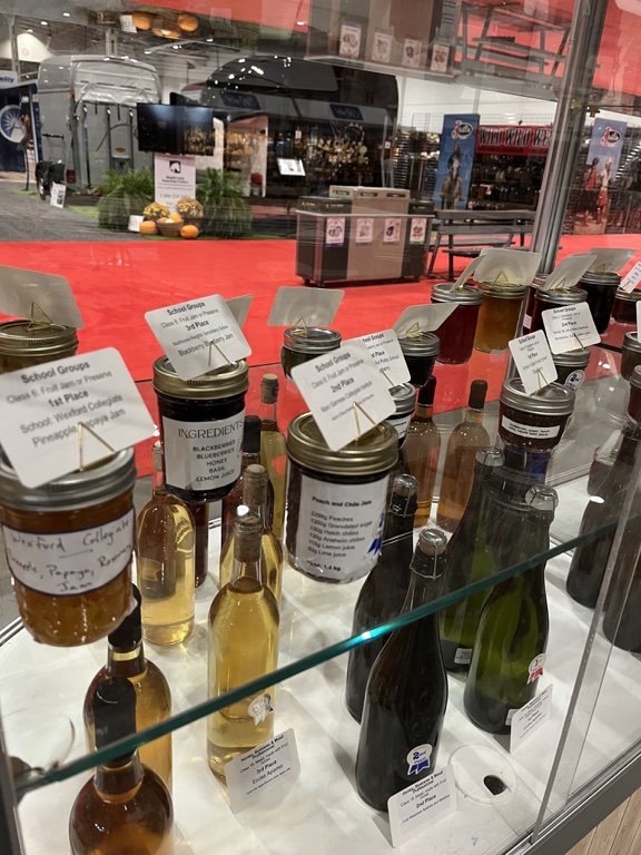 Jars of jelly sit in a row in a display case at the Royal Agricultural Winter Fair as part of the Champion's Showcase. The jars feature the school's name and placement in the competition. Each jar includes a descriptor of the ingredients included in the jelly recipe. 