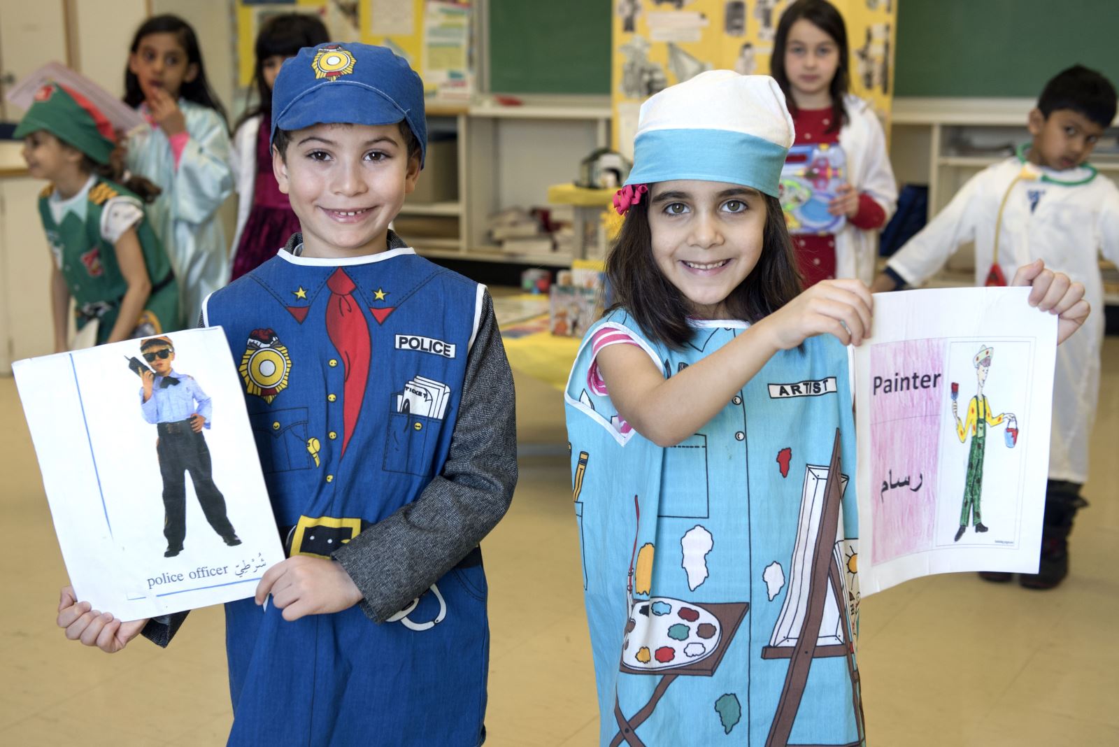 Two students in our ILE Arabic class dressed up and holding up their work with students standing in the background.