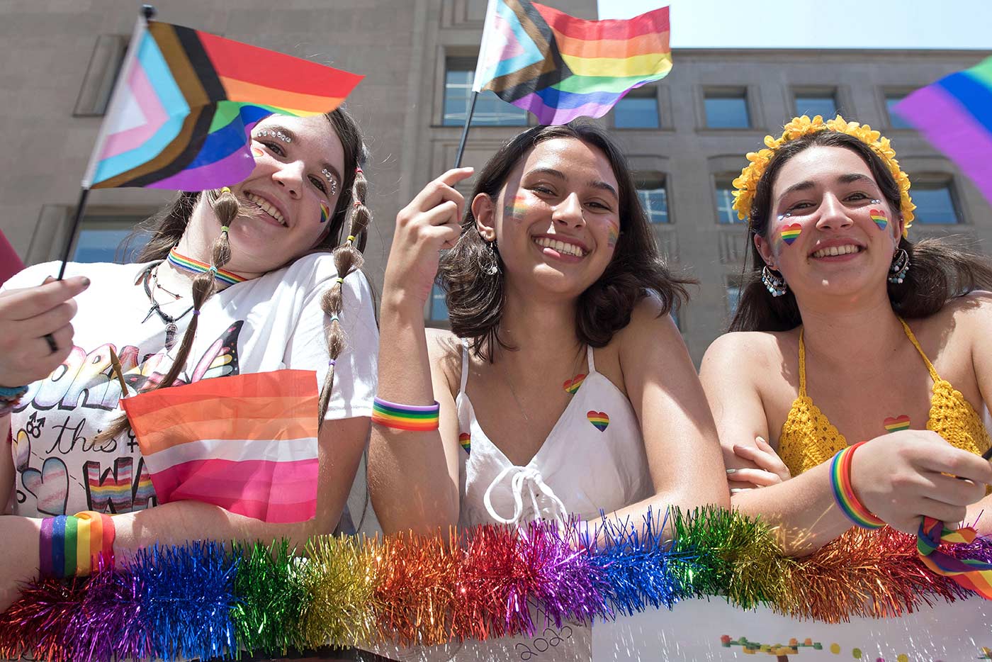 Three students holding Pride flags and smiling