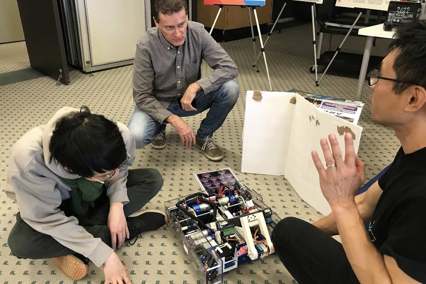 Two educators and student discussing the robotics project that is on the floor beside them
