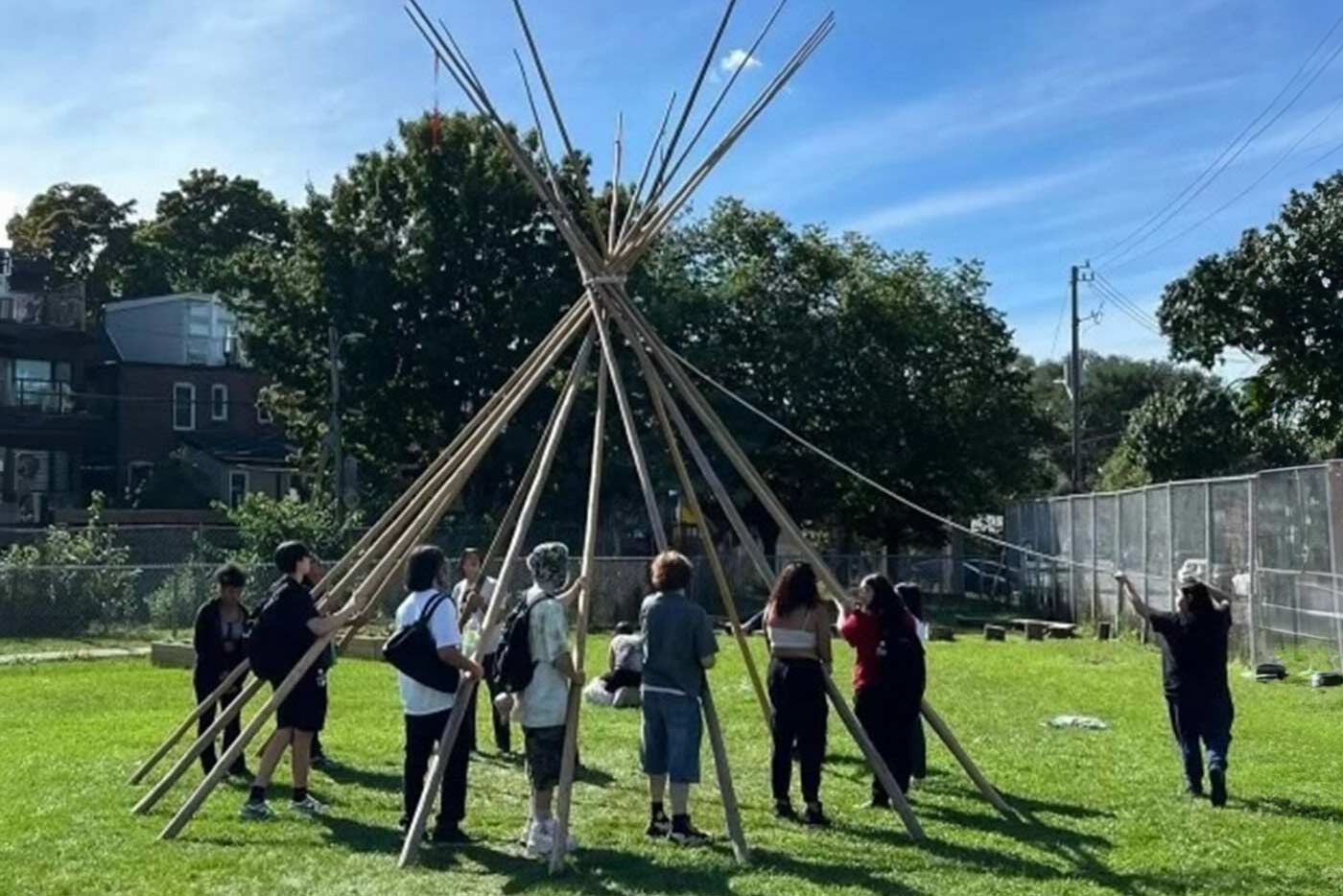 Students stand holding the pieces of a wooden frame for a tipi