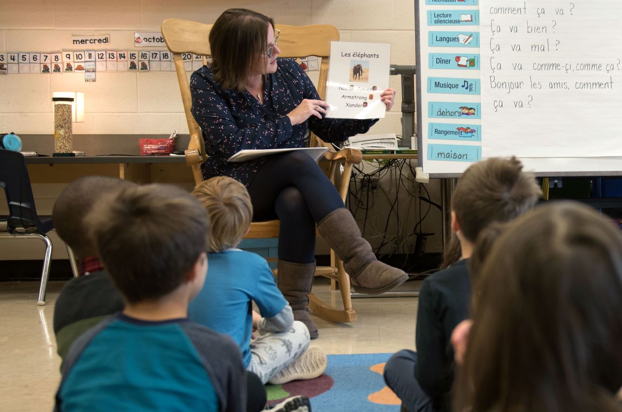 Educator reads French worksheet to students sitting on the carpet